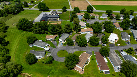Aerial view of a tranquil rural community featuring various Mobile, Prefab, Manufactured houses situated near lush green fields and trees. The landscape shows harmonious blend of residences farmland.の写真素材