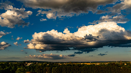 The sky glows with various shades as fluffy clouds gather above a vibrant green landscape during sunset. The horizon features rolling hills and hints of distant farmland.の写真素材