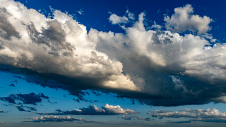 Vast clouds gather and disperse in a vibrant blue sky, creating striking patterns and shapes in the late afternoon light, showcasing natures beauty and ever-changing weather.の写真素材