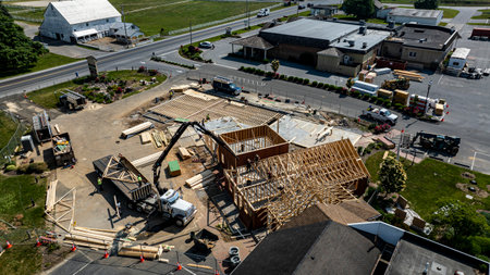 A construction project is progressing with workers actively framing a new building at a commercial location. The structure has wooden frames and is set amidst a clear sky and green landscape.の写真素材