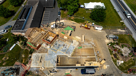 A construction project is progressing with workers actively framing a new building at a commercial location. The structure has wooden frames and is set amidst a clear sky and green landscape.の写真素材