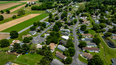 Aerial view of a tranquil rural community featuring various Mobile, Prefab, Manufactured houses situated near lush green fields and trees. The landscape shows harmonious blend of residences farmland.の写真素材