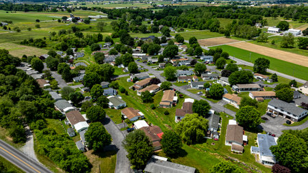 Aerial view of a tranquil rural community featuring various Mobile, Prefab, Manufactured houses situated near lush green fields and trees. The landscape shows harmonious blend of residences farmland.の写真素材