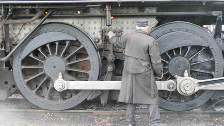 A steam engineer works diligently on the machinery of a vintage locomotive, ensuring its readiness...