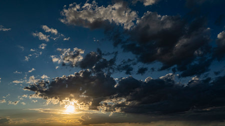 A vibrant sunset casts warm colors over expansive farmland, with lush green fields and patches of clouds creating a picturesque sky. The serene landscape reflects the tranquility of rural life.の写真素材