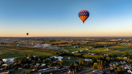 Hot air balloons float gracefully in the clear sky above a scenic countryside, capturing the tranquility of the early morning light as fields stretch below.の写真素材