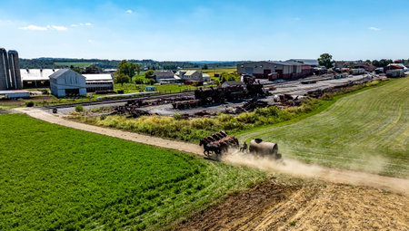 Wide View of Farmlands With Horses Pulling Manure Equipment Along a Dirt Road in Rural Setting, on a beautiful sunny day.の写真素材