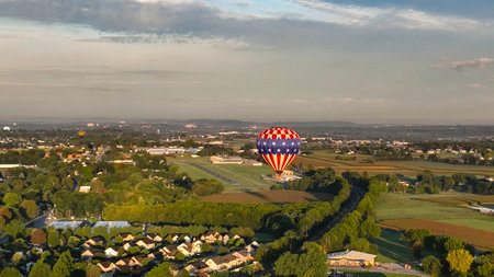 A vibrant hot air balloon rises above a lush green landscape as the sun sets, creating a picturesque view perfect for adventure and tranquility.の写真素材