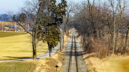 In a quiet winter setting, railway tracks extend into the distance between bare trees and open fields. The scene captures the essence of rural tranquility on a sunny day.の写真素材
