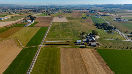An aerial view captures a vibrant countryside featuring expansive fields, barns, and winding rural roads, showcasing the beauty of agriculture during autumn.の写真素材