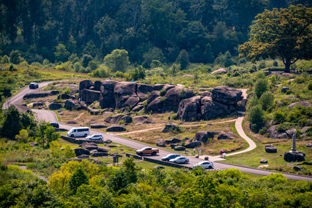 A view showcases a winding road through a lush landscape dotted with large boulders. Several vehicles are parked along the route, indicating visitor activity in the tranquil natural setting.の写真素材