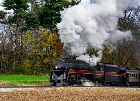 A vintage steam locomotive travels along countryside tracks, releasing clouds of smoke into the crisp autumn air. Colorful trees provide a backdrop as the train moves forward, evoking nostalgia.の写真素材