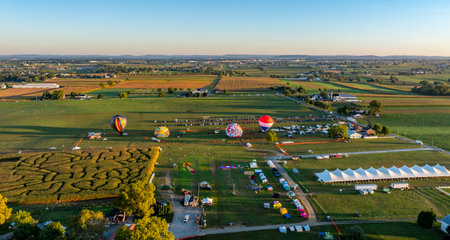 Hot air balloons take flight above expansive fields during a vibrant festival. The sky is painted with hues of orange as vendors and visitors enjoy various activities beneath.の写真素材