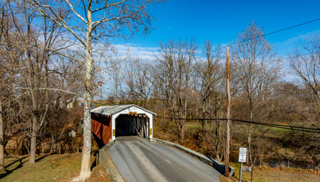 This location features a charming covered bridge set against a backdrop of leafless trees. The peaceful rural landscape provides a glimpse of nature on a clear day, enhancing the bridges beauty.の写真素材