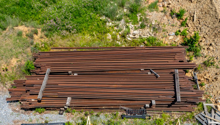 Rusty Rail Road Tracks Rails are neatly stacked on the ground at a construction site. The area is...