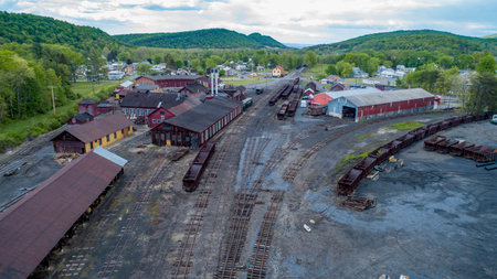 An expansive view of a historic train yard featuring multiple rail tracks and warehouses nestled in a lush green landscape. The bustling atmosphere reflects a spring afternoon with blue skies.の写真素材