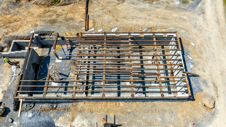 A construction site features a partially completed building framework situated on a gravel base. Construction workers are engaged in activities to erect the structure under a bright sky.の写真素材