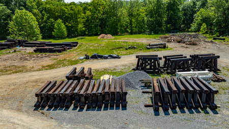 Stacks of Rail Road Train Trestles and heavy construction materials are organized on the ground in a rural setting. Surrounded by trees, the area has a clear sky and shows signs of ongoing development.の写真素材