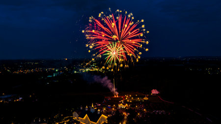 Bright fireworks burst in the night sky, casting colorful reflections over a city skyline. The sparkling display captures the excitement of a celebratory event, with lights twinkling below.の写真素材