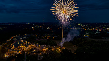 At dusk, a stunning display of fireworks fills the night sky above a lively festival. Twinkling lights adorn the ground, creating a magical atmosphere as spectators enjoy the festivities below.の写真素材