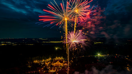 Vibrant fireworks burst in various colors above a crowd gathered at a picturesque outdoor site during an evening celebration. The lights reflect excitement and joy amid a dark sky.の写真素材