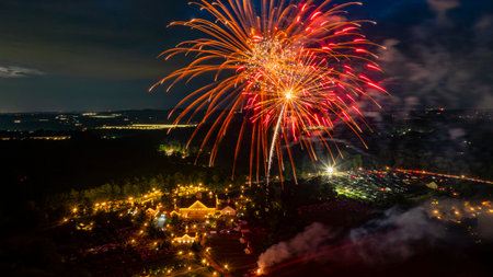 Vibrant fireworks burst overhead, illuminating the night sky above a lively event. Below, a crowd gathers around beautifully lit tents, enjoying the festivities and the stunning view.の写真素材