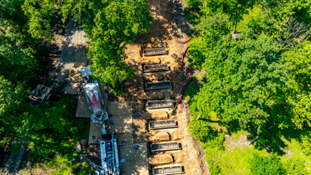 Heavy machinery is engaged in soil excavation at a construction site surrounded by trees. The area shows several prepared plots for development. It is daytime with clear visibility.の写真素材