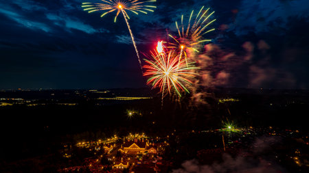 Bright fireworks burst in various colors above a bustling celebration location at night. The view captures the excitement of the crowd below, creating a festive atmosphere.の写真素材