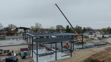 A construction site is active with workers using machinery and a crane. Steel beams are being lifted...