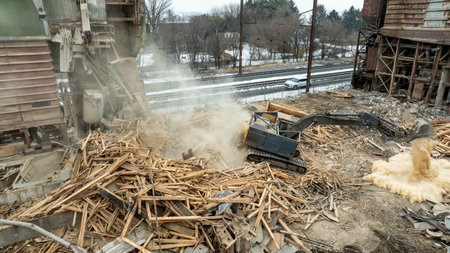 A large machine works at a construction site to remove debris. It moves wood and rubble while dust...