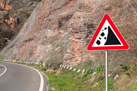 rockfall warning sign on the background of the crumbling hillside covered with protective metal meshの写真素材