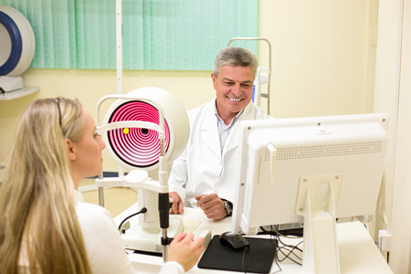 Optometry concept -  young woman having her eyes examined by an eye handsome elderly doctor. Topography of the corneaの写真素材