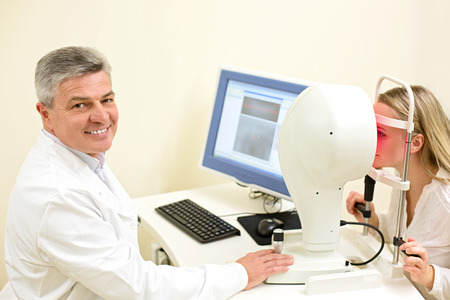 Optometry concept -  young woman having her eyes examined by an eye handsome elderly doctor. Topography of the corneaの写真素材