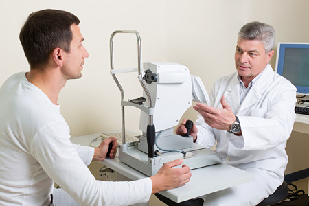 Optometry concept - man having his eyes examined by an eye  elderly doctor.の写真素材