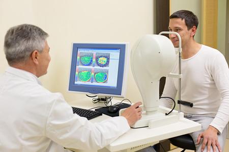 Optometry concept - man having his eyes examined by an eye  elderly doctor. Topography of the cornea.の写真素材