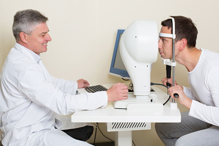 Optometry concept - man having his eyes examined by an eye  elderly doctor. Topography of the cornea.の写真素材
