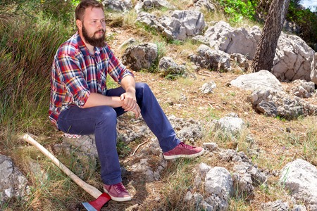 Portrait of an attractive young lumberjack who is resting sitting on a rockの写真素材