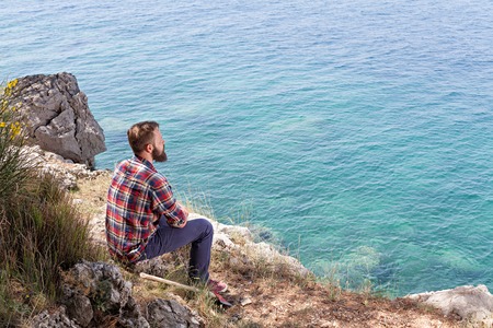 Portrait of an attractive young lumberjack who is resting sitting on a rockの写真素材