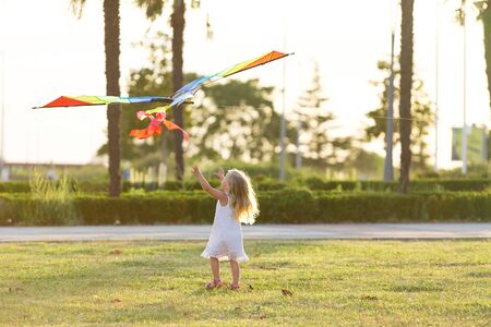 little girl in a white dress flying a kiteの写真素材