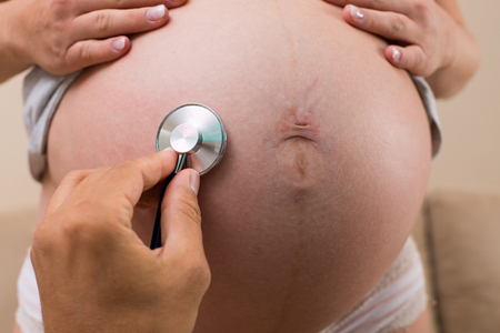 stethoscope listening to pregnant belly close upの写真素材