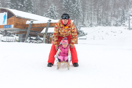 Dad and daughter posing with a sled in the winter outdoorsの写真素材