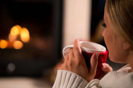 Woman is resting with cup of hot drink near the fireplaceの写真素材