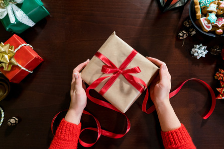 Woman hands wrapping xmas gifts into paper and tying them up with red threads