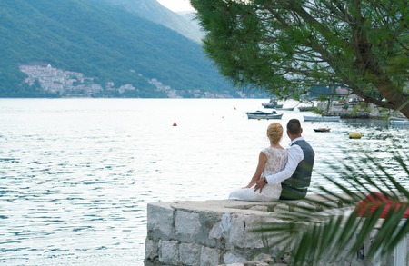 bride and groom sit on the pier hugging each other