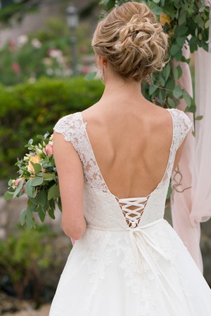 the bride in a wedding dress with a deep neckline stands on the background of greeneryの写真素材