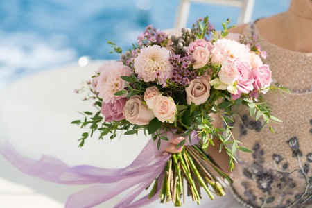 the bride holds a pink and lilac wedding bouquet in her arms against the background of the seaの写真素材