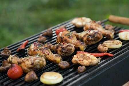 Closeup of a barbecue grill with chicken legs and vegetables, outdoors