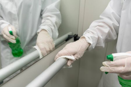 Woman using wet wipe and alcohol sanitizer spray to clean railing in the elevator. Disinfection,...