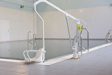 Lift for the descent of people with disabilities into the pool. On a blurred background, a swimming pool is visibleの写真素材