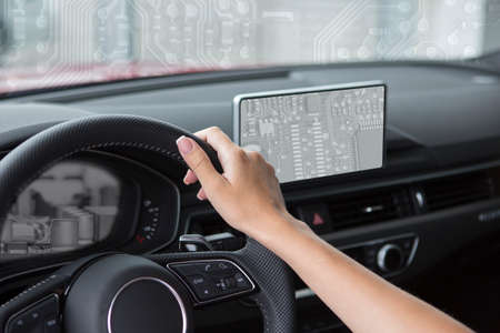 Woman is hands on the steering wheel of the car Selected focus The concept of using modern technology Collage Hands controlling the car against the backdrop of the electronic components of the computer.の写真素材